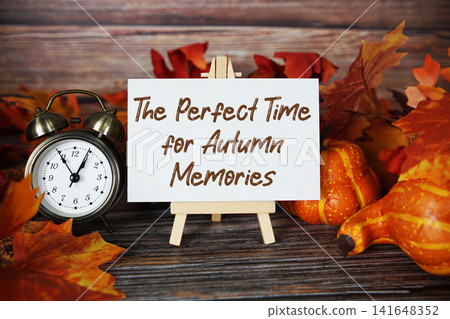 The Perfect Time for Autumn Memories text with alarm clock, maple leaf and pumpkins decoration on wooden background The Perfect Time for Autumn Memories text with alarm clock, maple leaf and pumpkins decoration on wooden background 141648352