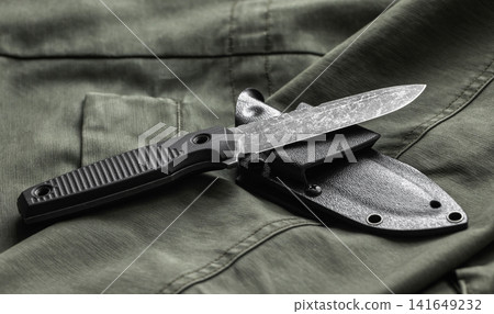 A tactical black knife with textured micarta handle and sheath rests on olive green fabric 141649232