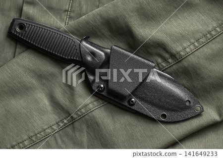 Tactical fixed-blade survival knife secured in a black Kydex sheath is on green fabric Tactical fixed-blade survival knife secured in a black Kydex sheath is on green fabric 141649233