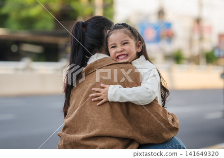 happy mother embracing daughter outdoors on city street 141649320