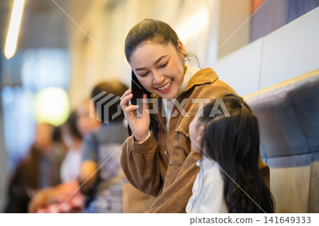 mother talking on a smartphone while her daughter looks at her at bus station in city at night mother talking on a smartphone while her daughter looks at her at bus station in city at night 141649333
