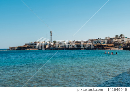 View of the Red Sea in Dahab, Egypt. Clear blue water with a bay featuring restaurants and hotels along the shoreline. Lighthouse Bay in the background. View of the Red Sea in Dahab, Egypt. Clear blue water with a bay featuring restaurants and hotels along the shoreline. Lighthouse Bay in the background. 141649946