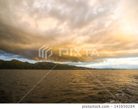 Stormy, cloudy sunset over Inle Lake in Myanmar, dramatic sky with dark rain clouds and warm evening light reflecting on the water around floating villages and stilt houses in Shan State Stormy, cloudy sunset over Inle Lake in Myanmar, dramatic sky with dark rain clouds and warm evening light reflecting on the water around floating villages and stilt houses in Shan State 141650284