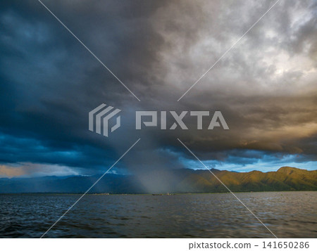 Stormy, cloudy sunset over Inle Lake in Myanmar, dramatic sky with dark rain clouds and warm evening light reflecting on the water around floating villages and stilt houses in Shan State Stormy, cloudy sunset over Inle Lake in Myanmar, dramatic sky with dark rain clouds and warm evening light reflecting on the water around floating villages and stilt houses in Shan State 141650286