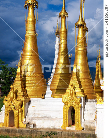 Golden Buddhist pagodas at Inle Lake, Myanmar, symbol of spiritual travel and cultural immersion, ancient stupas glowing in afternoon light under dramatic sky in Shan State Golden Buddhist pagodas at Inle Lake, Myanmar, symbol of spiritual travel and cultural immersion, ancient stupas glowing in afternoon light under dramatic sky in Shan State 141650297