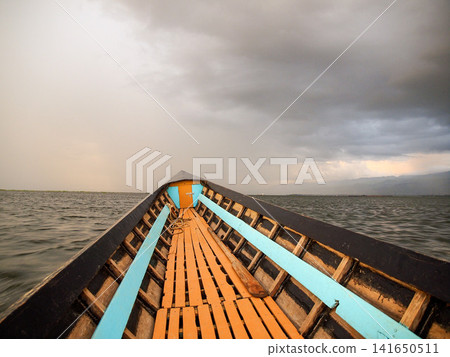 Bow of boat on Inle Lake in Myanmar under stormy cloudy sunset sky, dramatic travel scene with moody light over calm water and floating village atmosphere 141650511