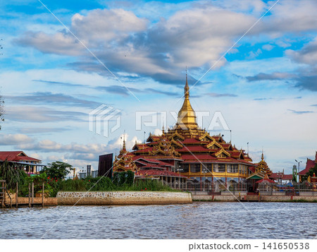 Golden pagoda by the water in Myanmar under a bright cloudy sky, scenic Buddhist temple with reflection and riverside view Golden pagoda by the water in Myanmar under a bright cloudy sky, scenic Buddhist temple with reflection and riverside view 141650538