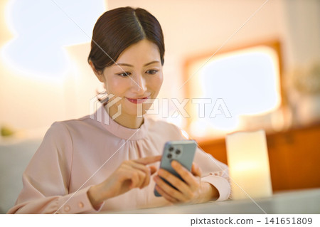 A woman in her 40s relaxing in her room at night and looking at her smartphone. A woman in her 40s relaxing in her room at night and looking at her smartphone. 141651809