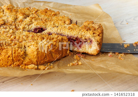 Homemade cherry crumb cake with golden streusel topping, cut into portions on parchment paper. Rustic German dessert 141652318