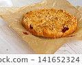 Whole round homemade cherry crumb cake with golden streusel topping resting on parchment paper on a light wooden table. Whole round homemade cherry crumb cake with golden streusel topping resting on parchment paper on a light wooden table. 141652324