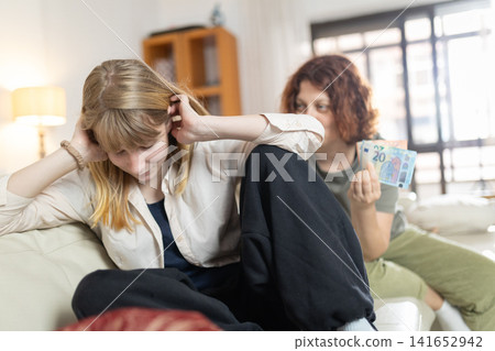 Young woman offering money to upset friend at home Young woman offering money to upset friend at home 141652942