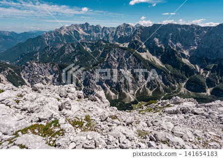 View from the middle Ponza mountain in Triglav National Park, Slovenia, looking over white rocky alpine valley routes and steep Julian Alps peaks with narrow hiking trails and dramatic mountain landsc View from the middle Ponza mountain in Triglav National Park, Slovenia, looking over white rocky alpine valley routes and steep Julian Alps peaks with narrow hiking trails and dramatic mountain landsc 141654183