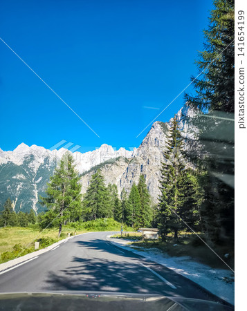 Stunning view on the Vrsic Pass in Triglav National Park, Slovenia, looking towards the rocky Julian Alps mountains with winding alpine road, green slopes and dramatic sky Stunning view on the Vrsic Pass in Triglav National Park, Slovenia, looking towards the rocky Julian Alps mountains with winding alpine road, green slopes and dramatic sky 141654199