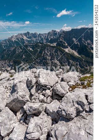 View from the middle Ponza mountain in Triglav National Park, Slovenia, looking over white rocky alpine valley routes and steep Julian Alps peaks with narrow hiking trails and dramatic mountain landsc View from the middle Ponza mountain in Triglav National Park, Slovenia, looking over white rocky alpine valley routes and steep Julian Alps peaks with narrow hiking trails and dramatic mountain landsc 141654212