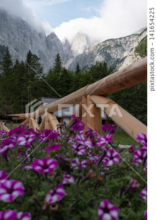 Planinski dom Tamar mountain hut in Planica Valley, Triglav National Park, Slovenia, view from Tamar house towards dramatic Julian Alps peaks with wooden fence and pink flowers Planinski dom Tamar mountain hut in Planica Valley, Triglav National Park, Slovenia, view from Tamar house towards dramatic Julian Alps peaks with wooden fence and pink flowers 141654225