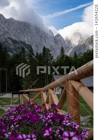 Planinski dom Tamar mountain hut in Planica Valley, Triglav National Park, Slovenia, view from Tamar house towards dramatic Julian Alps peaks with wooden fence and pink flowers Planinski dom Tamar mountain hut in Planica Valley, Triglav National Park, Slovenia, view from Tamar house towards dramatic Julian Alps peaks with wooden fence and pink flowers 141654228