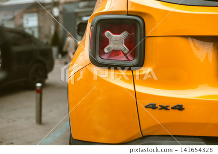 Close up detail of bright yellow compact SUV with 4x4 badge parked on urban street. Modern automotive design, contemporary city mobility and stylish crossover vehicle concept. Car trip. Urban scene. Close up detail of bright yellow compact SUV with 4x4 badge parked on urban street. Modern automotive design, contemporary city mobility and stylish crossover vehicle concept. Car trip. Urban scene. 141654328