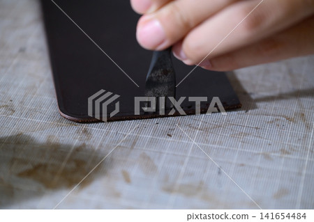 A leather craftsman's hands making sewing holes in leather with a four-pronged diamond awl. 141654484