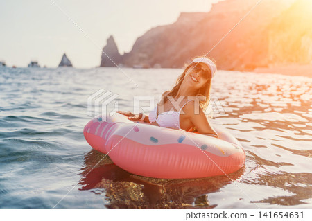 Woman, donut, ocean: Happy woman floats on an inflatable donut in the calm ocean during summer vacation. 141654631