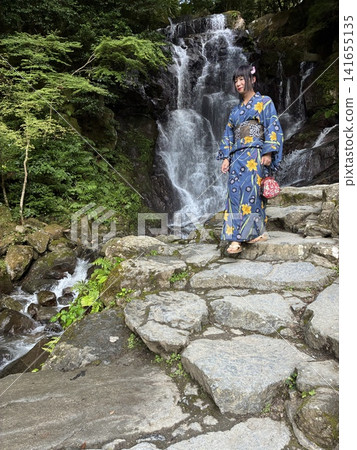 一位身穿浴衣的美麗女子沿著有瀑布的河岸漫步。 一位身穿浴衣的美麗女子沿著有瀑布的河岸漫步。 141655135