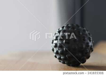 Textured black massage ball on a wooden surface. Textured black massage ball on a wooden surface. 141655308