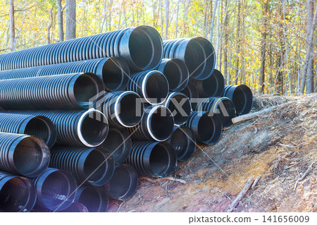 Black plastic waste PVC pipes are stacked in clearing among trees as workers prepare for construction. Black plastic waste PVC pipes are stacked in clearing among trees as workers prepare for construction. 141656009