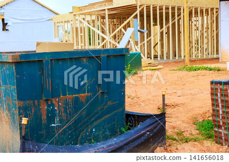 Workers build new structure at construction site blue dumpster sits in foreground. Workers build new structure at construction site blue dumpster sits in foreground. 141656018