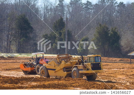 Large machinery moves dirt prepares ground for future development in forested setting. Large machinery moves dirt prepares ground for future development in forested setting. 141656027