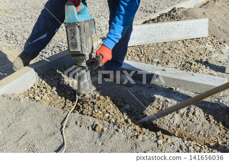 Worker is using jackhammer to break gravel at construction site Worker is using jackhammer to break gravel at construction site 141656036