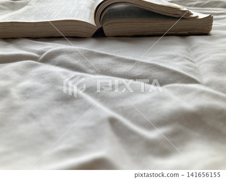 A book opened on a white sheet, creating a backdrop for reading time: a peaceful holiday enjoying reading. A book opened on a white sheet, creating a backdrop for reading time: a peaceful holiday enjoying reading. 141656155
