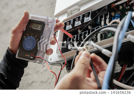 An electrician's hands measuring voltage with a tester. An electrician's hands measuring voltage with a tester. 141656236