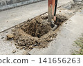 A hydraulic excavator excavates a paved road, causing soil and sand to pile up. 141656263
