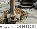 A close-up of soil being scooped up by the bucket of a hydraulic excavator. 141656264