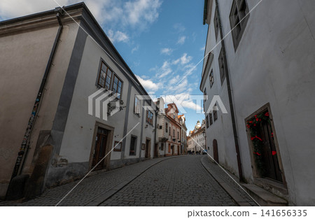 picturesque narrow historic street with traditional white buildings and cobblestone pavement under a bright blue sky with fluffy clouds in a charming European old town picturesque narrow historic street with traditional white buildings and cobblestone pavement under a bright blue sky with fluffy clouds in a charming European old town 141656335
