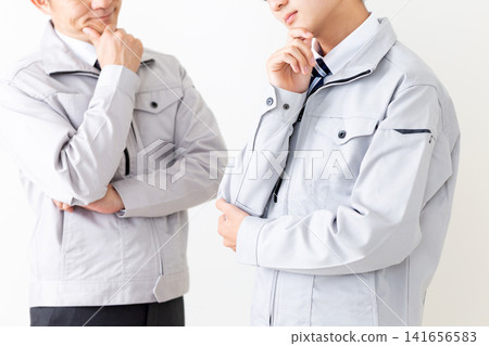 A young man and a middle-aged man in work clothes looking troubled. A young man and a middle-aged man in work clothes looking troubled. 141656583
