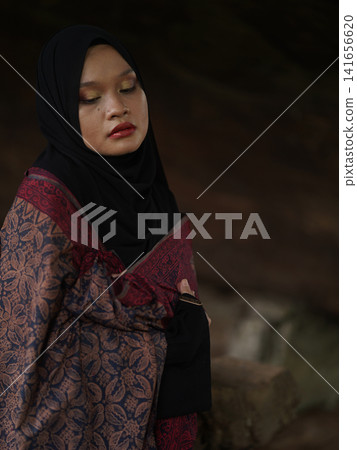 A fashionable young woman wearing a traditional black hijab and an elegant long red dress standing confidently against a weathered, vintage green door. Perfect for modest fashion, cultural, and lifest A fashionable young woman wearing a traditional black hijab and an elegant long red dress standing confidently against a weathered, vintage green door. Perfect for modest fashion, cultural, and lifest 141656620