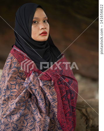 A fashionable young woman wearing a traditional black hijab and an elegant long red dress standing confidently against a weathered, vintage green door. Perfect for modest fashion, cultural, and lifest A fashionable young woman wearing a traditional black hijab and an elegant long red dress standing confidently against a weathered, vintage green door. Perfect for modest fashion, cultural, and lifest 141656622
