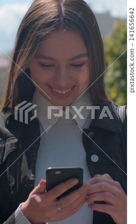 Vertical video. Young woman enjoying city streets, chatting with friends, using cellphone outdoors, beautiful sunset background. Vertical video. Young woman enjoying city streets, chatting with friends, using cellphone outdoors, beautiful sunset background. 141656642