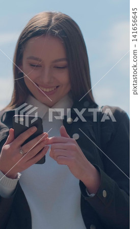 Vertical video. Young woman enjoying city streets, chatting with friends, using cellphone outdoors, beautiful sunset background. Vertical video. Young woman enjoying city streets, chatting with friends, using cellphone outdoors, beautiful sunset background. 141656645