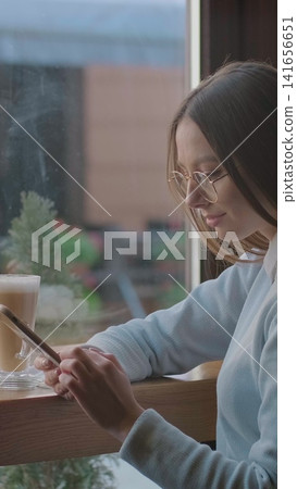 Vertical video. Woman using app on smartphone in cafe. Vertical video. Woman using app on smartphone in cafe. 141656651