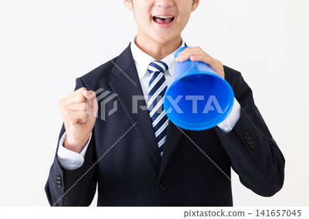 A young businessman in a suit cheering with a megaphone. A young businessman in a suit cheering with a megaphone. 141657045