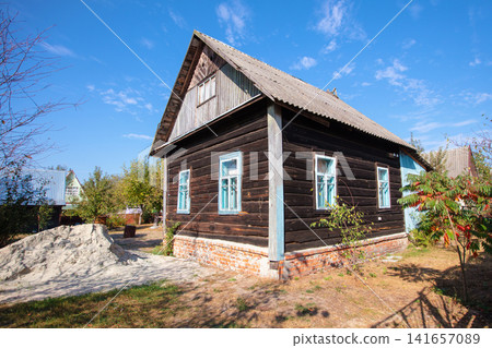 A small wooden village country house with a triangular roof. An old hut with a garden plot. A small wooden village country house with a triangular roof. An old hut with a garden plot. 141657089
