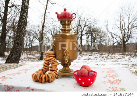 Winter scene with a samovar, pastries, and apples in a snowy landscape Winter scene with a samovar, pastries, and apples in a snowy landscape 141657144