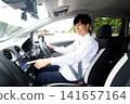 A young Asian man operating the car's navigation system inside the car. 141657164