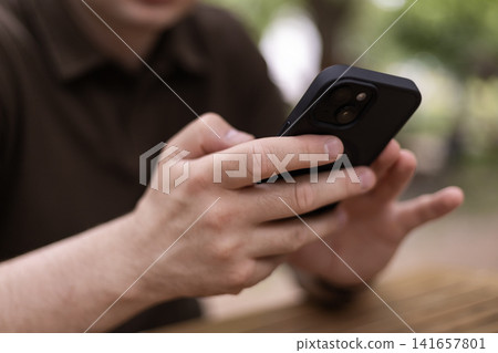 Man holding smartphone while sitting at outdoor cafe table Man holding smartphone while sitting at outdoor cafe table 141657801