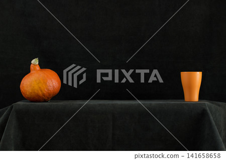 Still life with an orange pumpkin and an orange glass on a table Still life with an orange pumpkin and an orange glass on a table 141658658