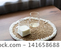 Ingredients for homemade iced coffee preparation with fresh milk and an empty glass on a natural woven placemat. Minimal kitchen scene showing the first step of making a refreshing summer coffee drink 141658688