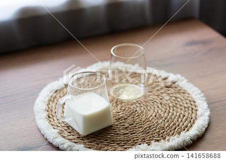 Ingredients for homemade iced coffee preparation with fresh milk and an empty glass on a natural woven placemat. Minimal kitchen scene showing the first step of making a refreshing summer coffee drink 141658688