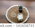 Ingredients for homemade iced coffee preparation with fresh milk and an empty glass on a natural woven placemat. Minimal kitchen scene showing the first step of making a refreshing summer coffee drink 141658733