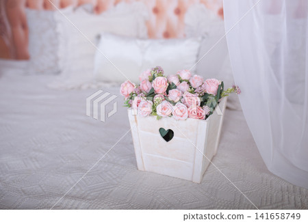 Decorative wooden box with pink flowers on bed in bright bedroom interior for cozy atmosphere Decorative wooden box with pink flowers on bed in bright bedroom interior for cozy atmosphere 141658749